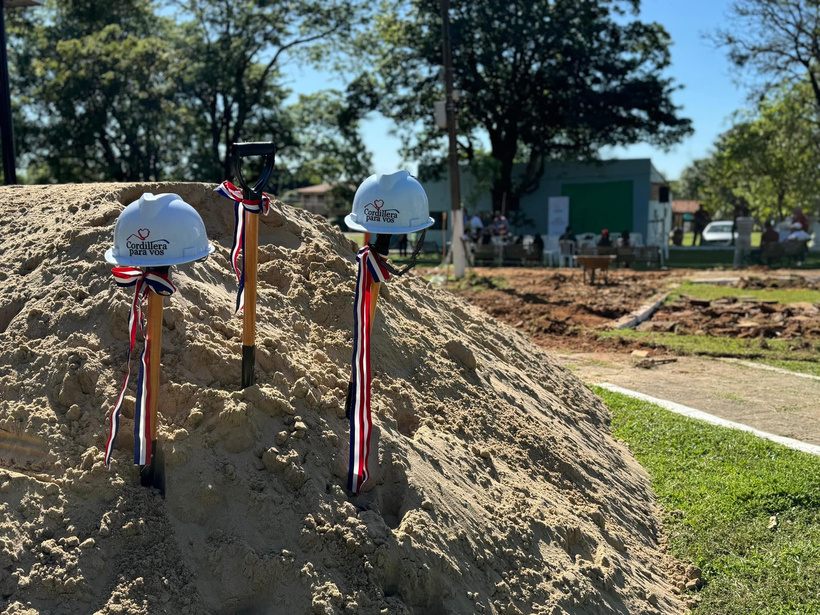 Cascos de obra y palas con cintas tricolores clavadas en un montículo de tierra durante el acto de inicio de una obra en el Departamento de Cordillera
